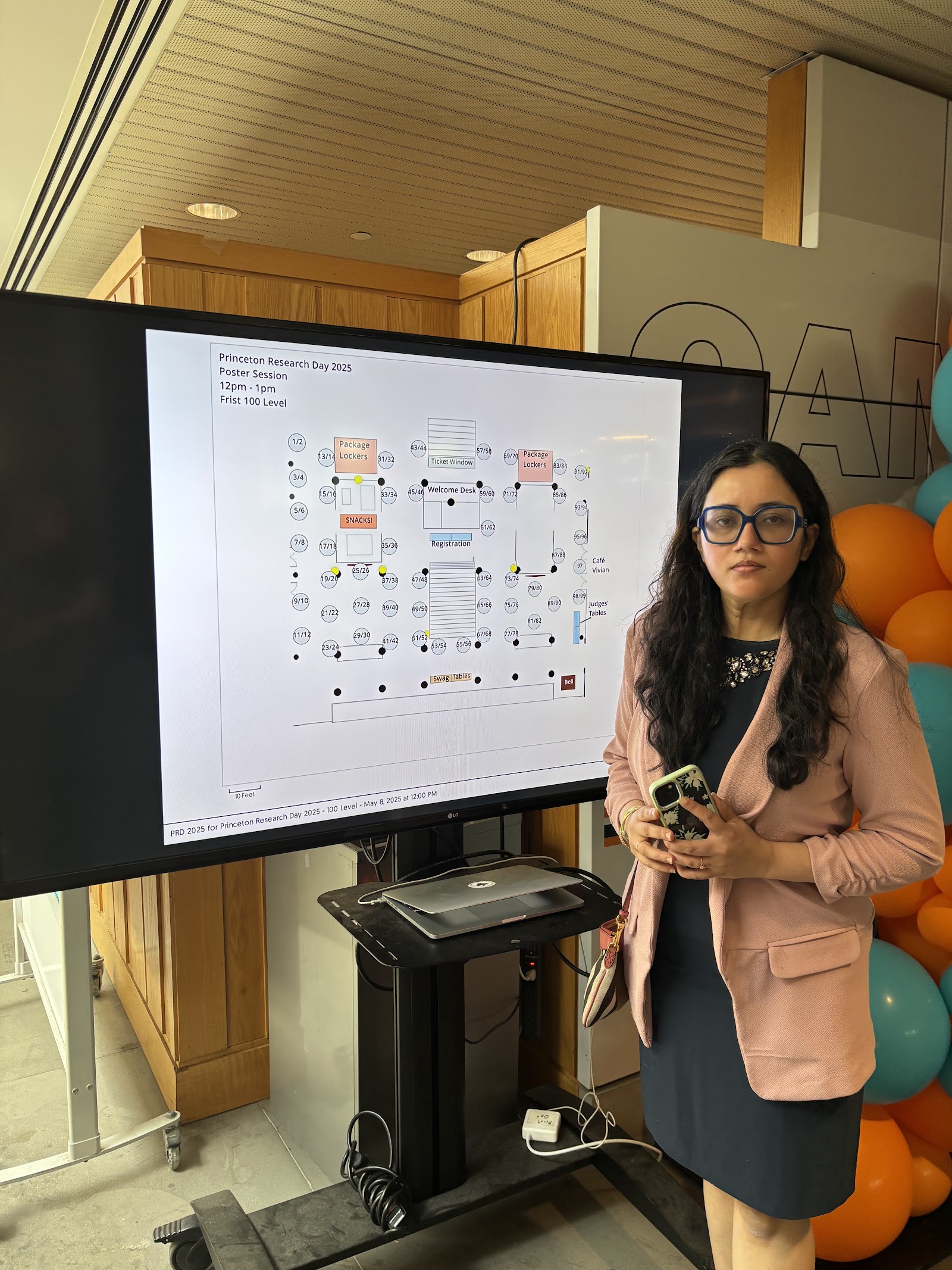 Shalvi beside a screen showing a numbered floor map of the poster garden.
