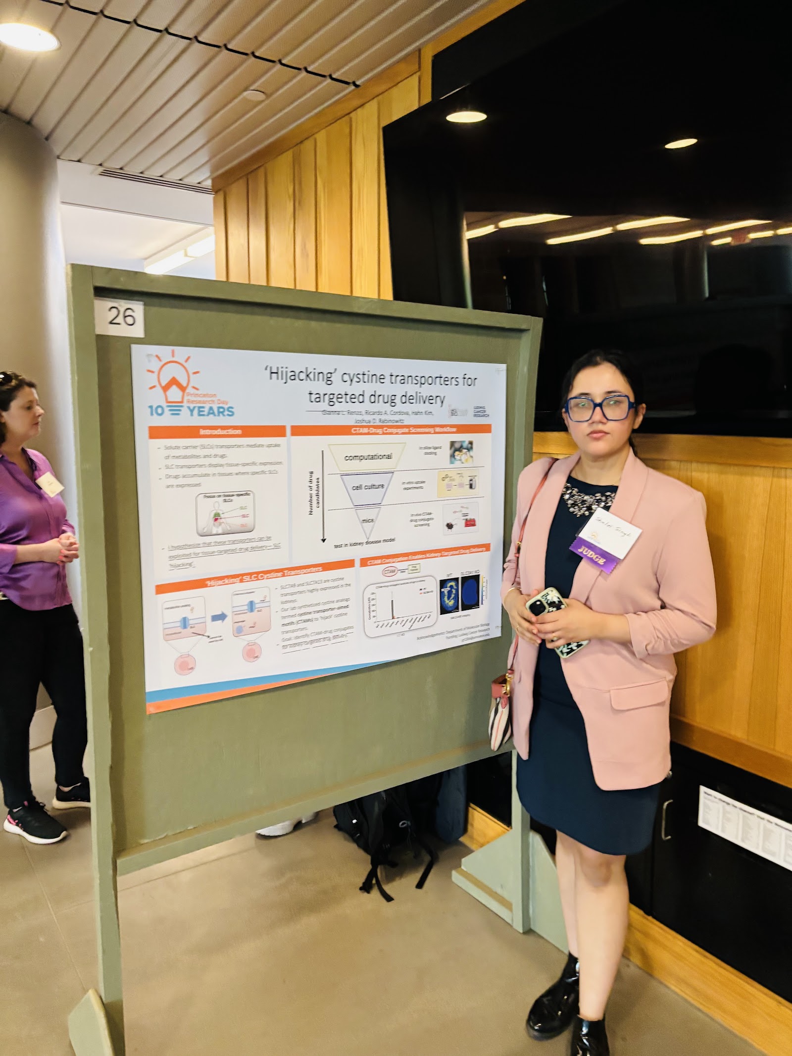 Shalvi next to poster 26, titled “‘Hijacking’ cystine transporters for targeted drug delivery.”