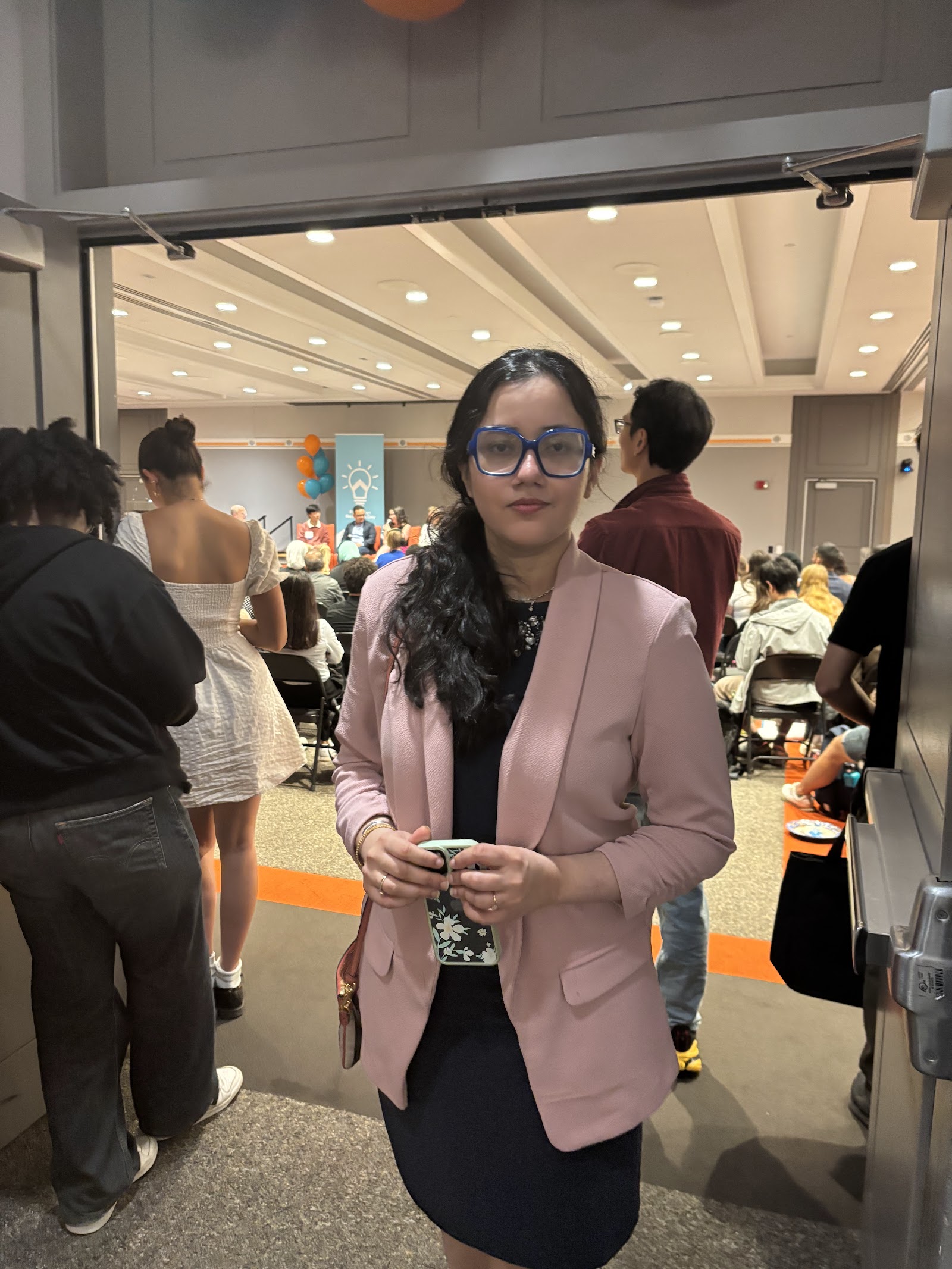 Shalvi holding a coffee in a doorway with the busy event room behind her.