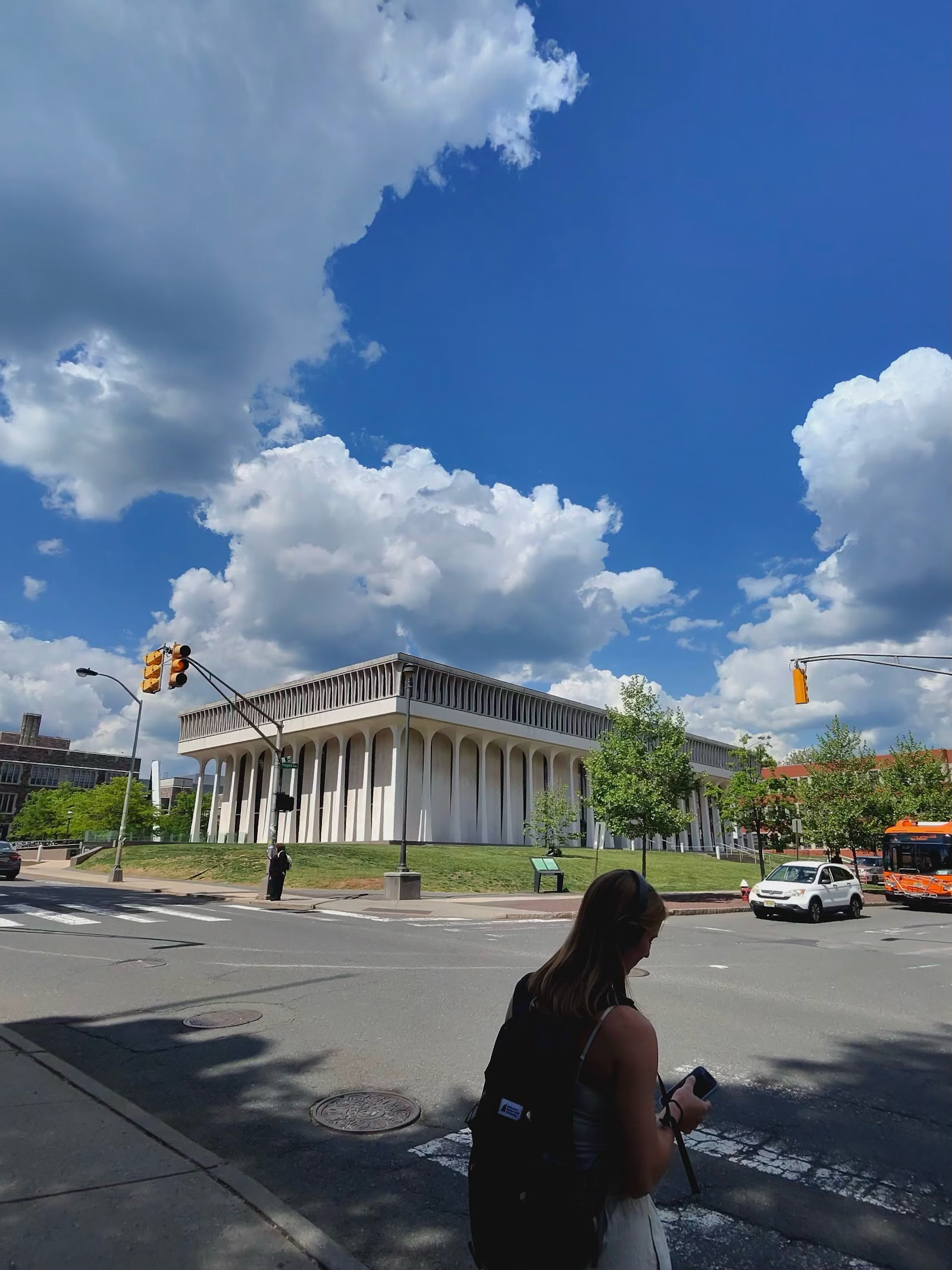A white colonnaded stone building across an intersection under a big cloud-filled sky.