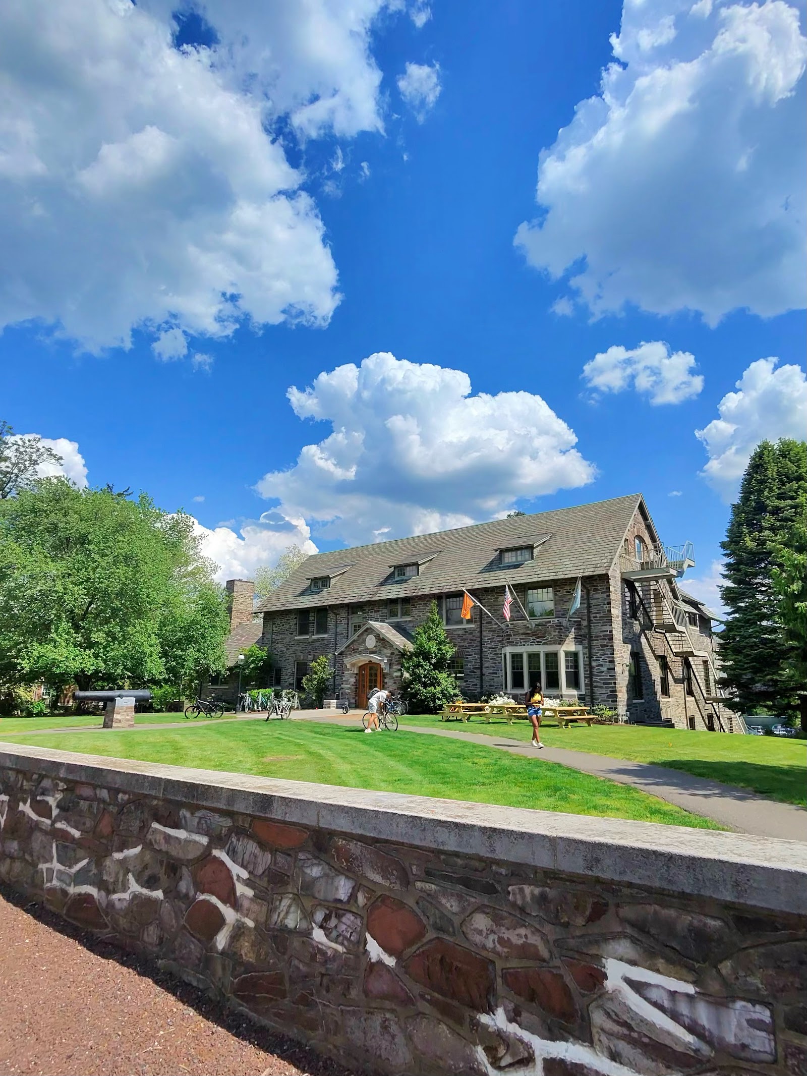 A stone gothic-style house with a peaked roof behind a low stone wall under a blue sky.