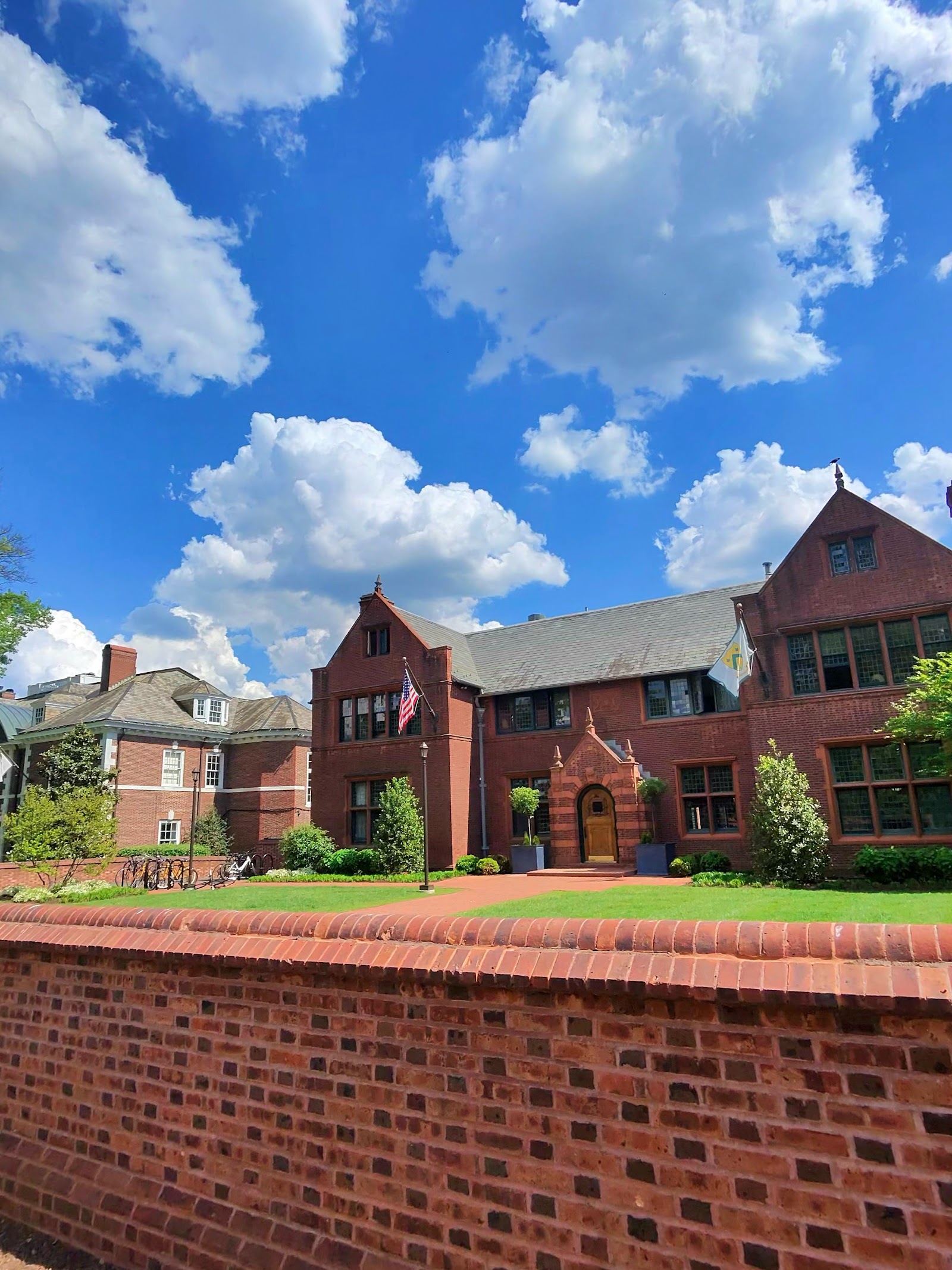 A large brick Georgian mansion behind a brick wall and manicured lawn.